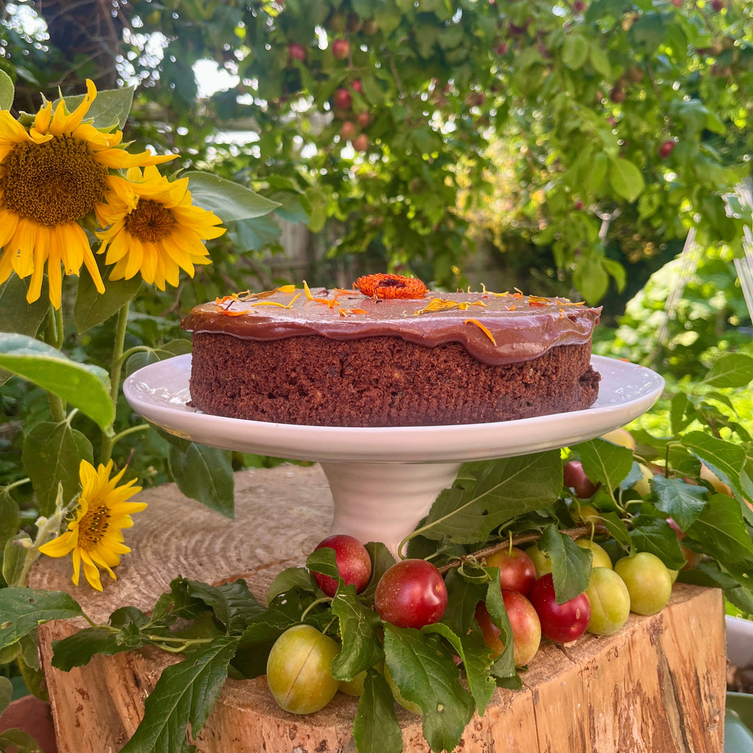Chocolate cake on a white stand with sunflowers and apples in an outdoor setting